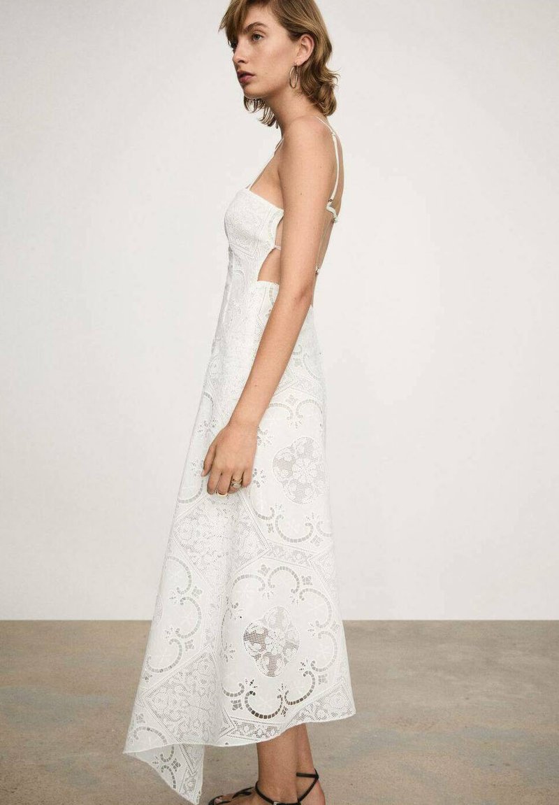 Biała koronkowa sukienka midi z wycięciami po bokach, cienkimi ramiączkami i asymetrycznym dołem. Posiada misternie wykonane wzory oraz lekką teksturę.