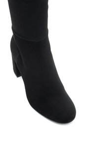 Czarny botek do kostki wykonany z miękkiego zamszu, z blokowym obcasem i zaokrąglonym noskiem. Szwy akcentują elegancki design.