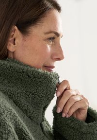 Groene fleece pullover met hoge kraag, met een gestructureerd, pluizig oppervlak. De kraag is gedeeltelijk met een rits gesloten; geen zichtbare patronen of hardware.