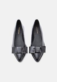 Must have mustast nahast teravad varbad, millel on suur dekoratiivne lips üle varvaste valgel taustal.