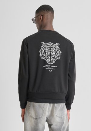 Sudadera negra con gráfico de tigre blanco en la parte posterior, puños y dobladillo de canalé. Presenta un cuello redondo y un corte relajado.