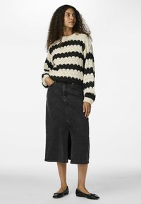 Dicker gestrickter Pullover in Creme mit schwarzen Streifen, kombiniert mit einem schwarzen Denim-Midikleid mit einem Schlitz vorne. Schwarze Ballerinas runden das Outfit ab.