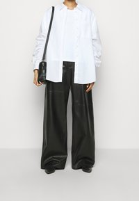 Bílá košile s dlouhými nařasenými rukávy, doplněná o oversize černé kožené kalhoty a malou černou crossbody kabelku.