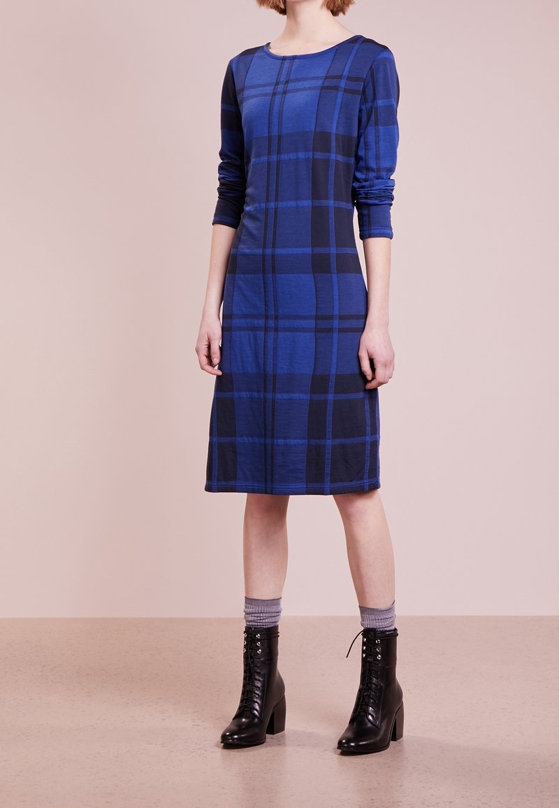 Langärmliges, blaues kariertes Kleid mit Rundhalsausschnitt, knielangem Schnitt und aus weichem Baumwollmix. Getragen mit schwarzen Schnürstiefeletten.