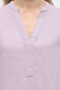 Femme portant un chemisier en lin violet clair avec un col en V et un col montant, montrant la partie supérieure de la poitrine et du cou.