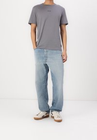 Grijze katoenen t-shirt met "REPLAY" logo, lichtblauwe denim spijkerbroek en witte sneakers met zilveren accenten. Casual pasvorm, standaard ontwerp.