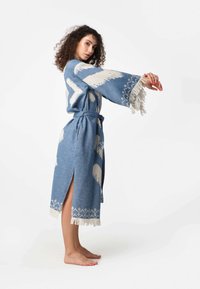 Modrá textúrovaná róba s bielymi vzormi, má široké rukávy, viazaný pás, bočné rozparky a strapcové detaily na spodnom leme.