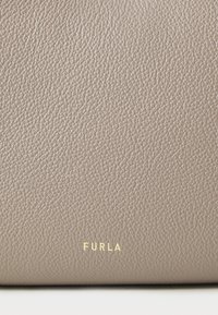 Sac Furla en cuir taupe doux et texturé avec un grain subtil. Détail du logo en or en bas. Forme simple et rectangulaire.