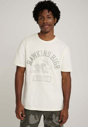 Kremowy t-shirt z nadrukiem przedstawiającym jeźdźca rodeo i tygrysa. Krótkie rękawy, okrągły dekolt i miękki bawełniany materiał.