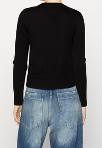 Maglione nero a maglia con scollatura rotonda e maniche lunghe, abbinato a jeans di denim blu chiaro sbiaditi con una toppa sulla tasca posteriore.