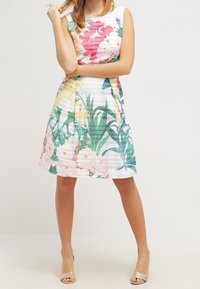 Robe à imprimé floral avec un corsage ajusté, des manches courtes et une jupe évasée. Principalement blanche avec des accents roses, jaunes et verts. Texture lisse.