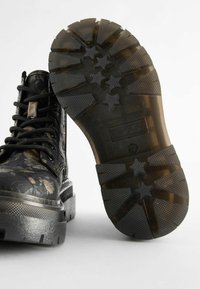 Bottes de combat à motif floral noir avec semelles texturées. Dotées de lacets robustes et d'un épais talon en caoutchouc pour la durabilité.