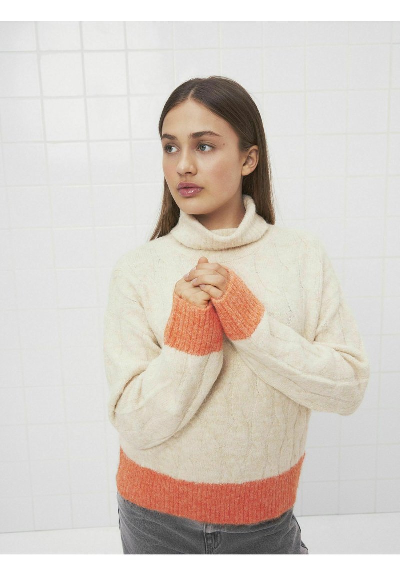 Krämfärgad tröja med ribbade orangea muddar och nederkant, med hög hals och strukturerad flätad design.