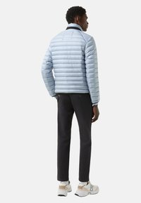 Light blue puffer jacket with quilted design and black collar, paired with dark pants and white sneakers. Smooth texture and casual fit.