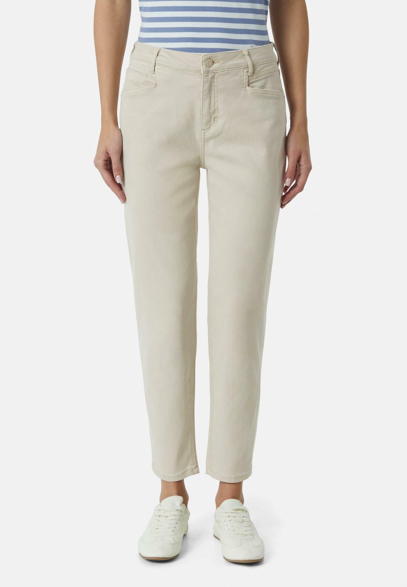 Beige Denimjeans mit slim fit, fünf Taschen und Knopfverschluss. Kombiniert mit weißen Sneakers und einem blau-weiß gestreiften Oberteil.