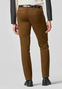 Braune Slim-Fit-Hosen mit glatter Textur, Gesäßtaschen und einem schwarzen Gürtel. Getragen mit schwarzen Knöchelstiefeln.