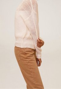 Pull en tricot rose clair, caractérisé par une maille lâche et des poignets côtelés. Associé à un pantalon beige à jambes droites avec un détail de poche arrière.