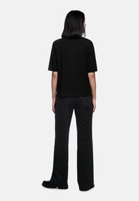 Black oversized t-shirt with short sleeves, paired with dark gray patterned jeans featuring a star motif and flared shape. Black footwear.