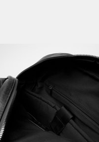 Bolso de cuero negro con apertura con cremallera, que presenta un forro interior texturizado, bolsillo interior con cremallera y un soporte de correa de tela.