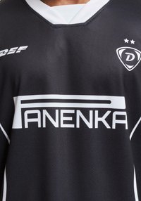 Juoda sportinė marškinė su baltomis detalėmis, su V formos apykakle ir logotipu "D" su dviem žvaigždėmis viršuje. Pagaminta iš tekstūruoto, kvėpuojančio audinio.