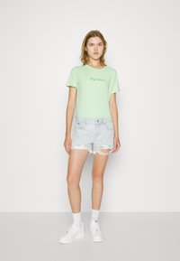 Zelena majica kratkih rukava u mentol boji s izvezenim natpisom "Pepe Jeans" u zelenoj boji. Uparena s svijetloplavim poderanim trapericama. Bijele tenisice i čarape.