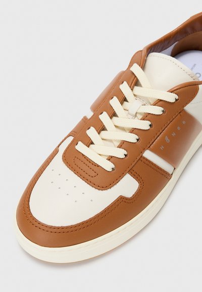 Bruna lädersneakers med krämfärgade detaljer, som har en perforerad tå, platta krämfärgade snörning och en minimalistisk design med subtil branding.