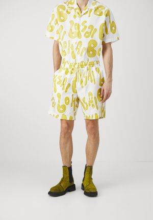 Weißes Kurzarmhemd und Shorts-Set mit einem gelben abstrakten Muster. Kombiniert mit strukturierten gelben Knöchelstiefeln mit schwarzen Akzenten.
