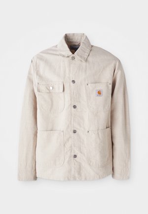 Chaqueta de trabajo beige hecha de tejido duradero, cuenta con un cierre de botones a presión, dos bolsillos en el pecho y un parche con el logo en el bolsillo izquierdo.