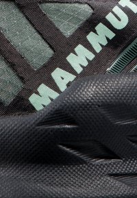 Calzature Mammut con una suola nera texture, tomaia in rete verde scuro e dettagli del logo verde chiaro. Progettate per resistenza e aderenza.