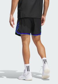 Pantalones cortos deportivos negros con acentos en verde y azul, con un dobladillo escalonado. Combinados con zapatillas blancas y calcetines de rayas.