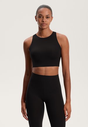 Čierny crop top s vysokým výstrihom a širokými ramienkami, vyrobený z hladkého materiálu. V páre s čiernymi legínami s vysokým pásom, obidva majú minimalistický dizajn.