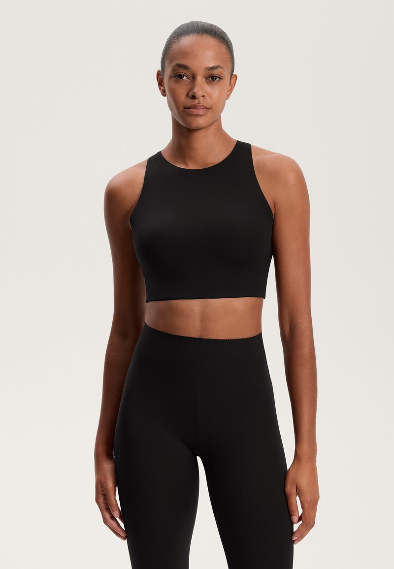 Črni kratki top z visokim ovratnikom in širokimi naramnicami, izdelan iz gladkega materiala. Usklajen z visokimi črnimi legicami, oboje ima minimalistični dizajn.