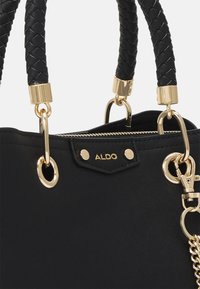 Sort håndtaske med flettede håndtag, guldfarvede detaljer, lynlåslukning og en guldkædeapplikation, mærket "ALDO" på forsiden.