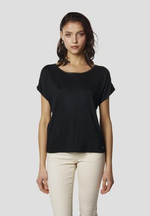 Črna majica s kratkimi rokavi in okroglim izrezom, okrašena z metalnimi zakovicami ob robu. Iz mehke, lahke tkanine.