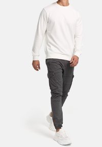 Sweat-shirt blanc et pantalon cargo gris avec poches, associés à des baskets blanches. La tenue présente une coupe décontractée et des poignets élastiques.