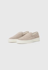 Beige semskede slip-on sko med rund tå, sydd detaljering og hvit gummisåle. Jevn tekstur med minimalistisk design.