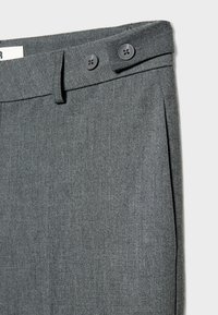Taille de pantalon en tissu gris avec deux boutons noirs et une passants de ceinture, montrant une partie d'une poche latérale et un détail de la ceinture.