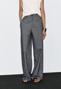Grau gestreifte weite Hose mit hoher Taille, ausgestattet mit einem Knopfverschluss vorne und seitlichen Taschen, kombiniert mit einem weißen ärmellosen Top.