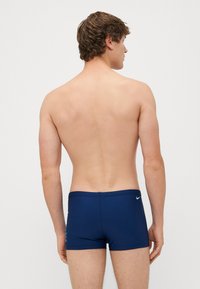 Mörkblå badshorts i stretchigt tyg, med en åtsittande passform, medelhög midja och en liten logotypdetalj på baksidan.