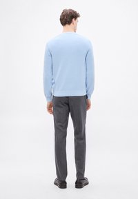 Világoskék pulóver bordázott textúrával, kerek nyakkivágással és hosszú ujjal, sötétszürke, szabott nadrággal és fekete cipővel párosítva.