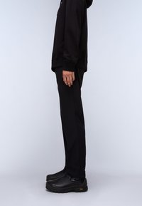 Black hooded sweatshirt, black pants, and black slip-on shoes. Smooth fabric, relaxed fit, side view, minimalist design.