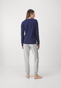 Granatowa koszulka z długim rękawem i okrągłym dekoltem, połączona z jasnoszarymi spodniami dresowymi z brązowym paskiem po boku, obie z miękkiego materiału.