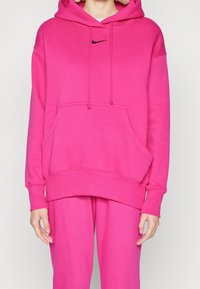 Felpa rosa con tasca a marsupio frontale, lacci e un piccolo logo Nike nero sul petto. Tessuto morbido e polsini a costine.