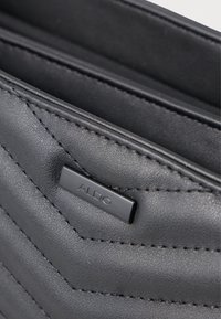 Czarna torba z syntetycznej skóry w wzór chevron, z subtelną tabliczką z logo ALDO i kontrastowymi szwami. Wnętrze ma podział na dwa przegrody.