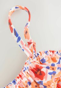 Virágmintás fürdőruha felső, narancs, kék és rózsaszín árnyalatok keverékével. Állítható pántokkal, redőzött anyaggal és varrott díszítéssel.