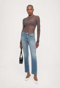 Transparante bruine lange mouw top, blauwe rechte jeans, witte puntige schoenen en zwarte handtas. Gladde textuur, aansluitende silhouet.