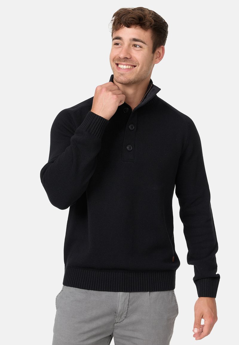 Suéter de punto negro con cuello alto, detalles de botones, puños y dobladillo acanalados. Textura suave diseñada para brindar calidez y comodidad.