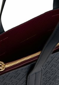 Zwarte faux leer handtas met een gegraveerd patroon, bordeauxrood interieur, gouden rits en logo in het goud afgedrukt op de voering.