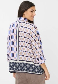 Blusa distintiva con motivi geometrici in rosa, blu e navy. Tessuto leggero, maniche a 3/4, design del bordo a contrasto.