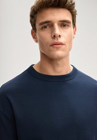 Granatowa bluza wykonana z miękkiej mieszanki bawełny, z okrągłym dekoltem i gładką fakturą, o minimalistycznym designie i bez widocznych wzorów.